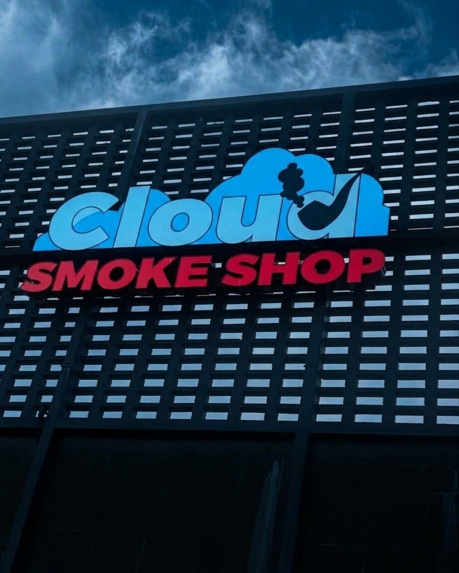 Cloud Smoke Shop's blue and red storefront sign mounted on the store's dark facade under an open Tallahassee sky.