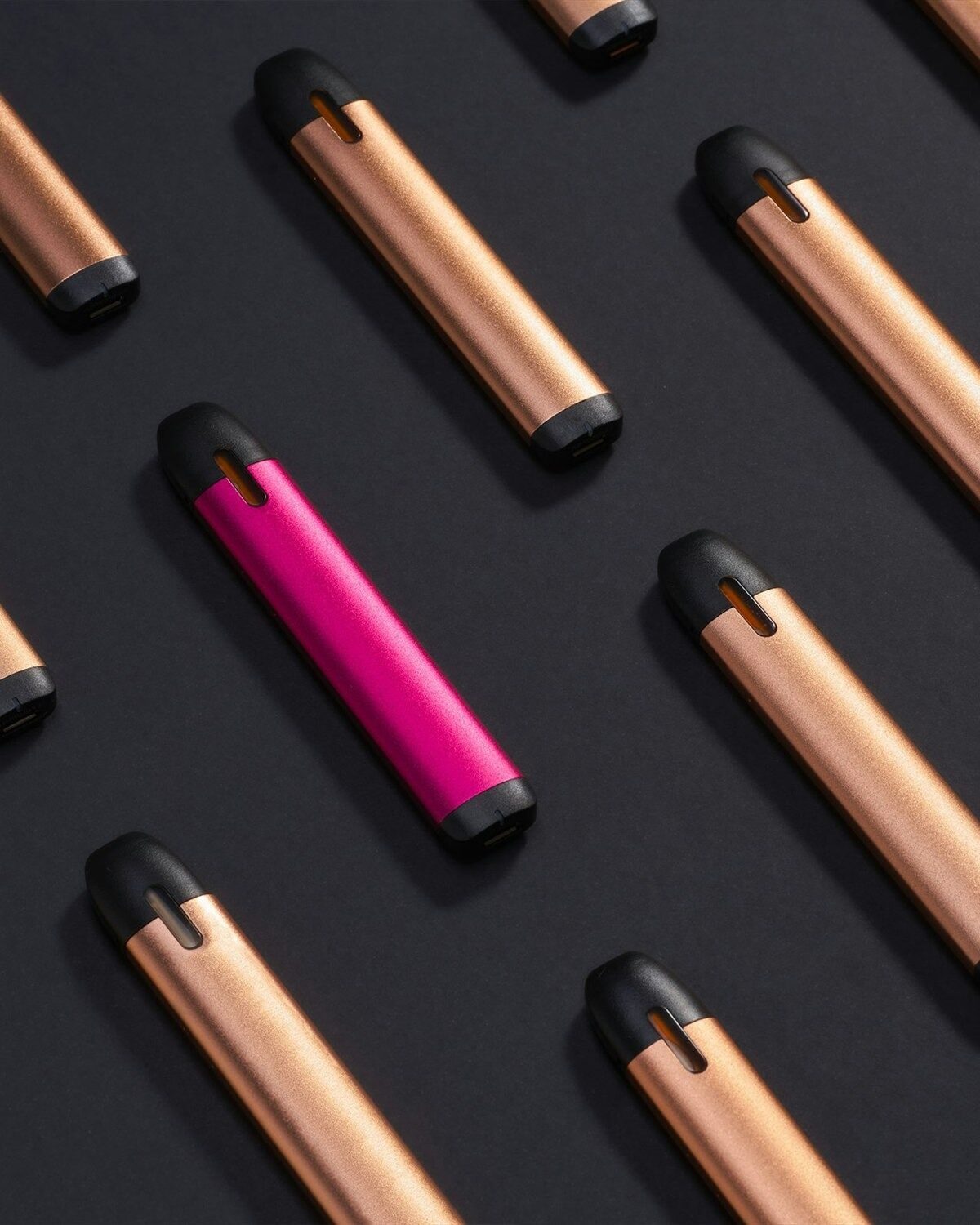 Rows of copper and one pink disposable vape pen laid out on a dark surface.